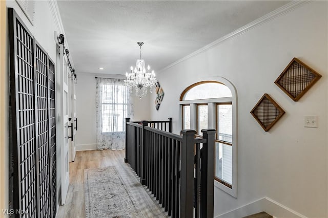 corridor featuring a chandelier, a wealth of natural light, light wood-type flooring, and ornamental molding