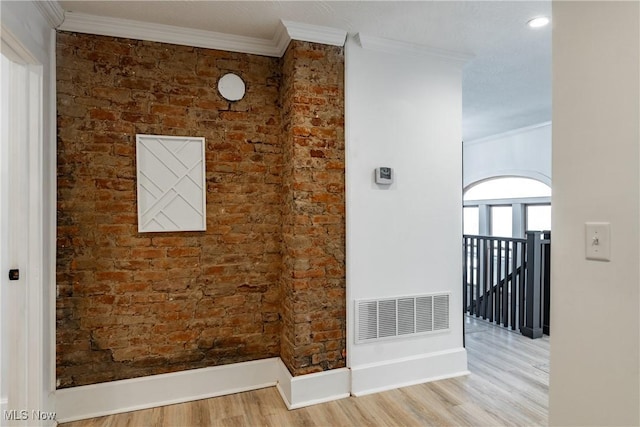 interior space with wood-type flooring, ornamental molding, and brick wall