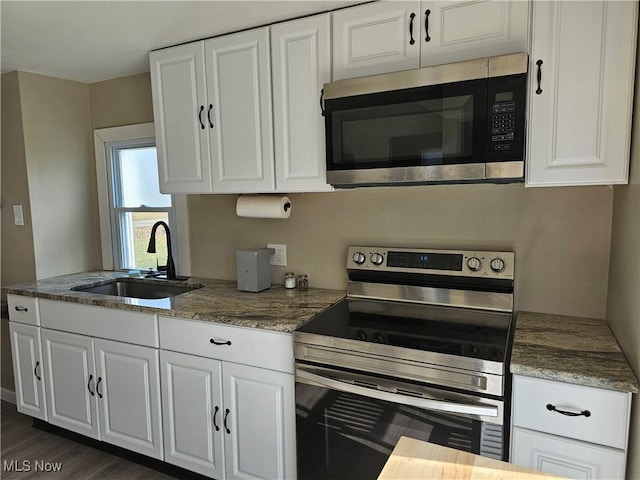 kitchen featuring sink, dark hardwood / wood-style flooring, dark stone counters, white cabinets, and appliances with stainless steel finishes