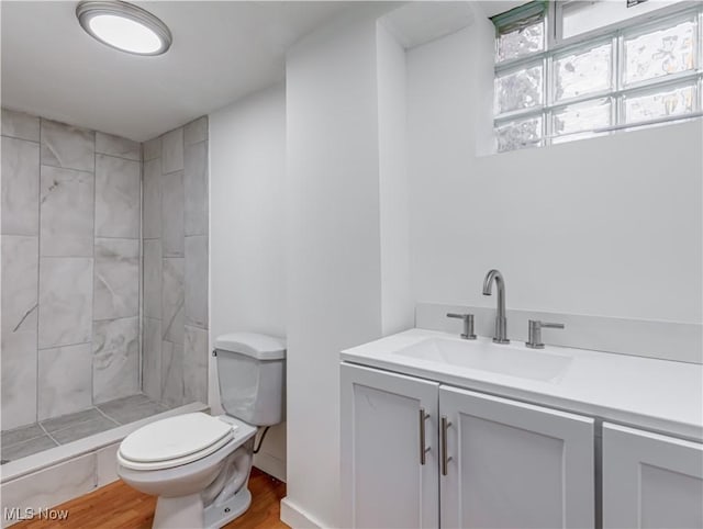 bathroom with tiled shower, hardwood / wood-style floors, vanity, and toilet