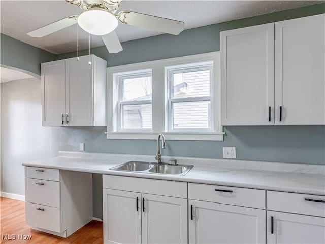 kitchen with ceiling fan, white cabinetry, sink, and light hardwood / wood-style flooring