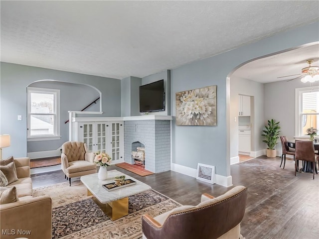 living room featuring ceiling fan, a textured ceiling, a wealth of natural light, and a brick fireplace