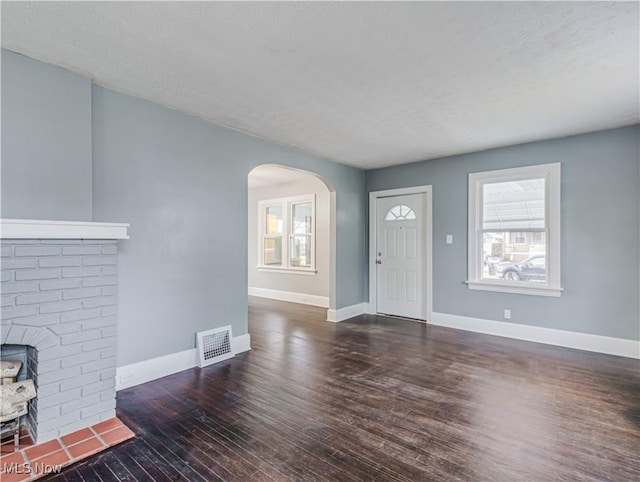 living room featuring a textured ceiling, dark wood-type flooring, and a brick fireplace