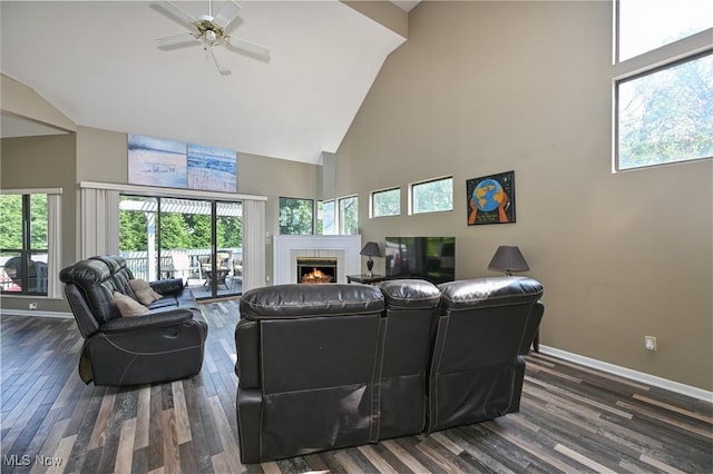 living room with a towering ceiling, dark hardwood / wood-style flooring, ceiling fan, and a tiled fireplace