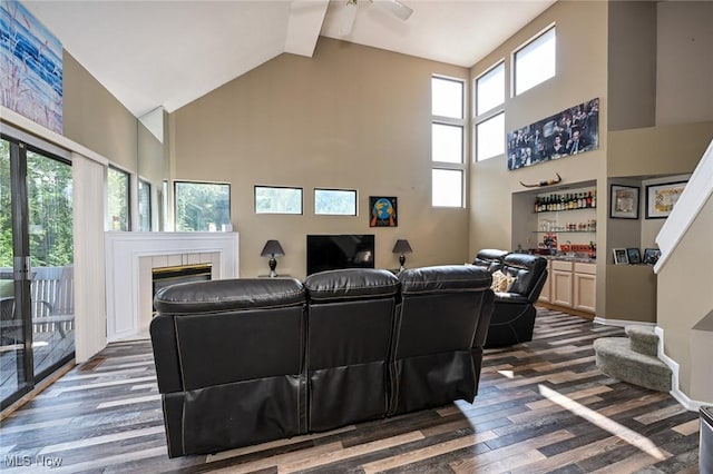 living room featuring dark hardwood / wood-style flooring, ceiling fan, indoor bar, high vaulted ceiling, and a tiled fireplace