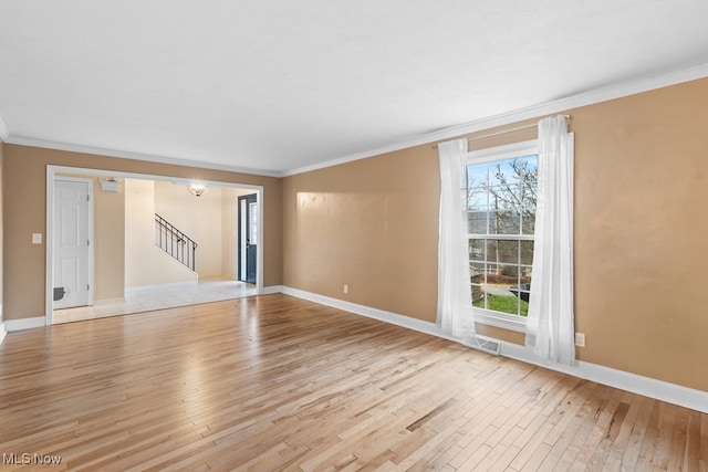 spare room featuring light wood-type flooring, baseboards, stairway, and crown molding