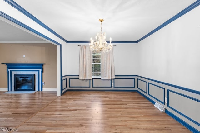 unfurnished dining area featuring a notable chandelier, visible vents, light wood-style floors, ornamental molding, and a glass covered fireplace