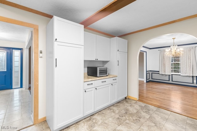 kitchen with white cabinets, crown molding, hanging light fixtures, light stone countertops, and a chandelier