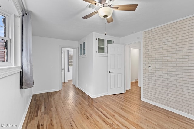 empty room with light wood-type flooring, baseboards, ceiling fan, and brick wall