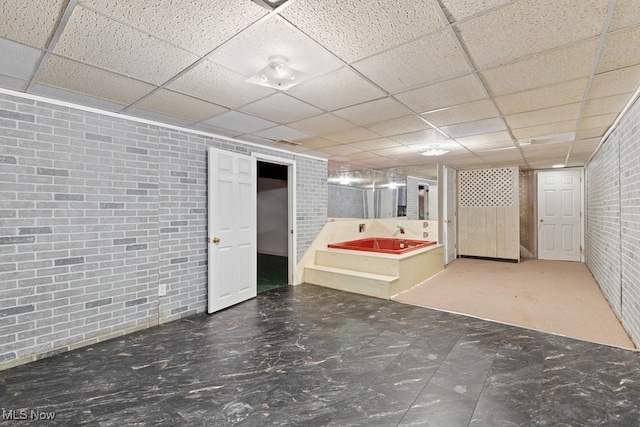 finished basement featuring a paneled ceiling and brick wall