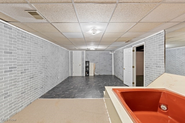 basement with a drop ceiling and brick wall