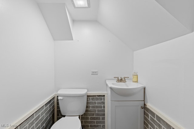 half bath with toilet, vanity, tile walls, vaulted ceiling, and wainscoting