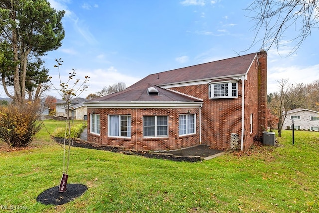 view of side of home with brick siding, a yard, and central AC unit