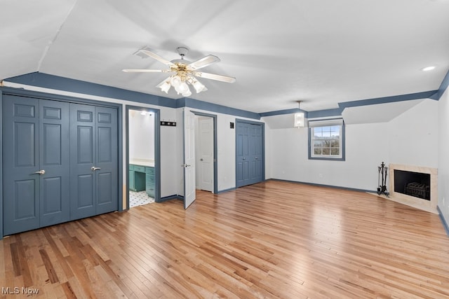 interior space with two closets, a fireplace with flush hearth, ceiling fan, light wood-type flooring, and baseboards