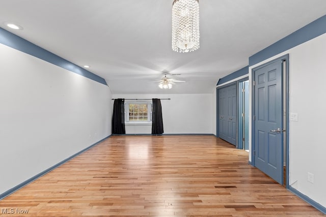 unfurnished room featuring light wood-style floors, vaulted ceiling, baseboards, and ceiling fan with notable chandelier