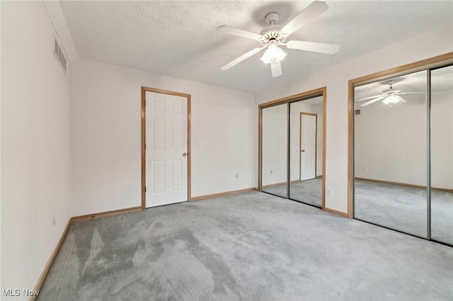 unfurnished bedroom featuring ceiling fan, light colored carpet, a textured ceiling, and two closets