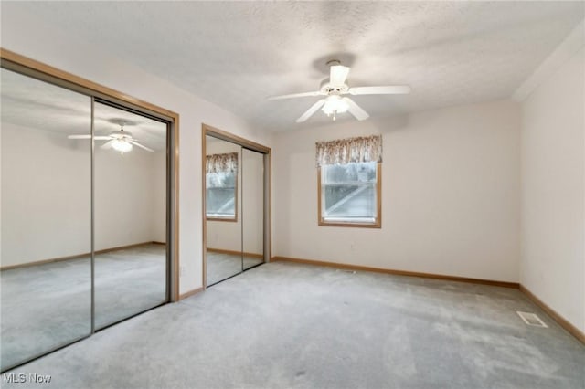 unfurnished bedroom featuring a textured ceiling, ceiling fan, carpet, and two closets