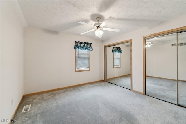 unfurnished bedroom featuring a textured ceiling, ceiling fan, light carpet, and two closets