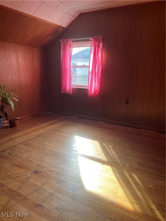 bonus room with hardwood / wood-style floors, wood walls, and lofted ceiling