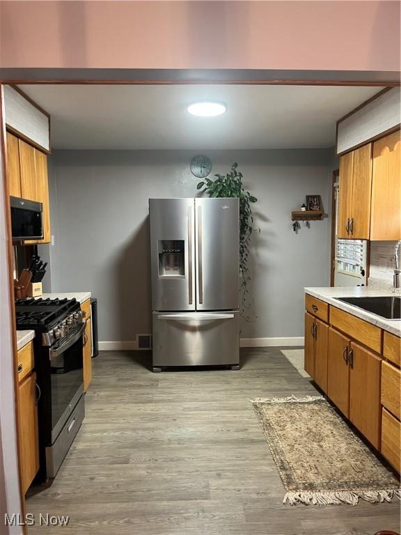 kitchen featuring stainless steel fridge, sink, black range with gas cooktop, and light wood-type flooring