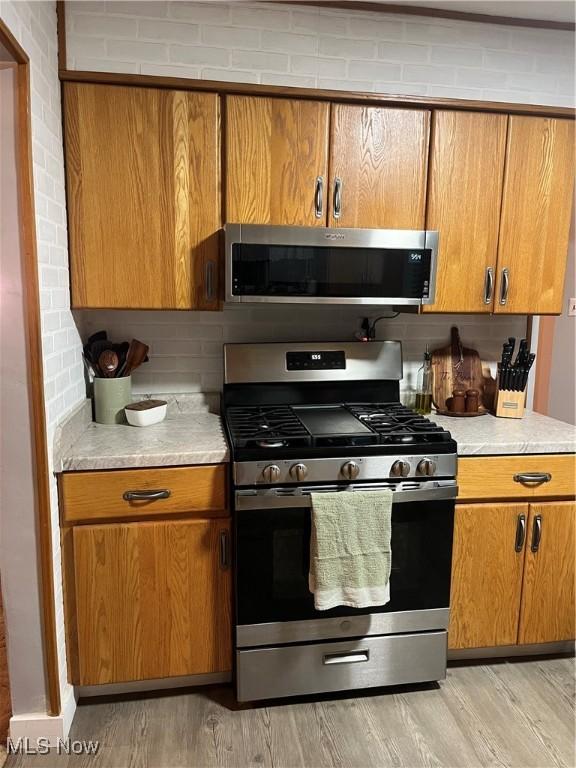 kitchen with backsplash, appliances with stainless steel finishes, and light hardwood / wood-style flooring