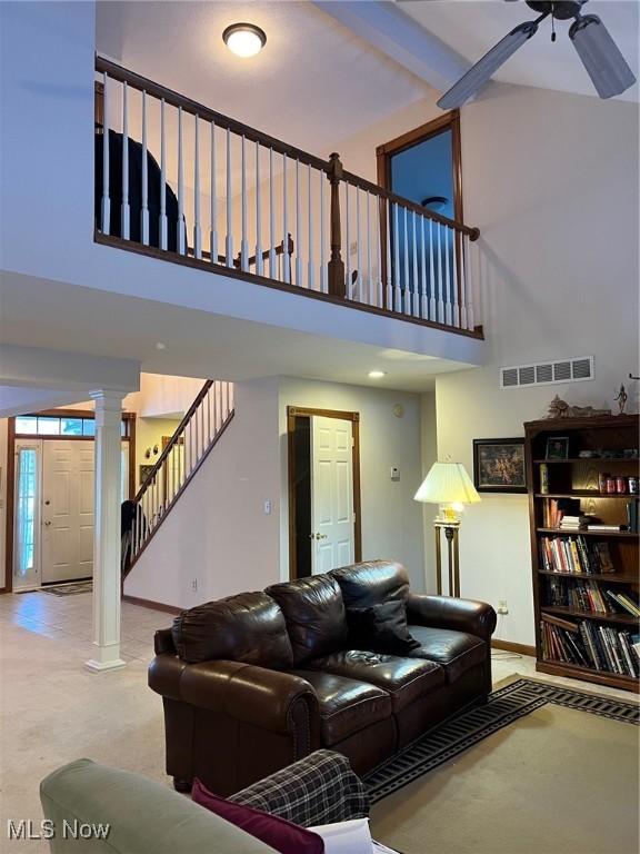 carpeted living room with beam ceiling, ceiling fan, ornate columns, and a towering ceiling