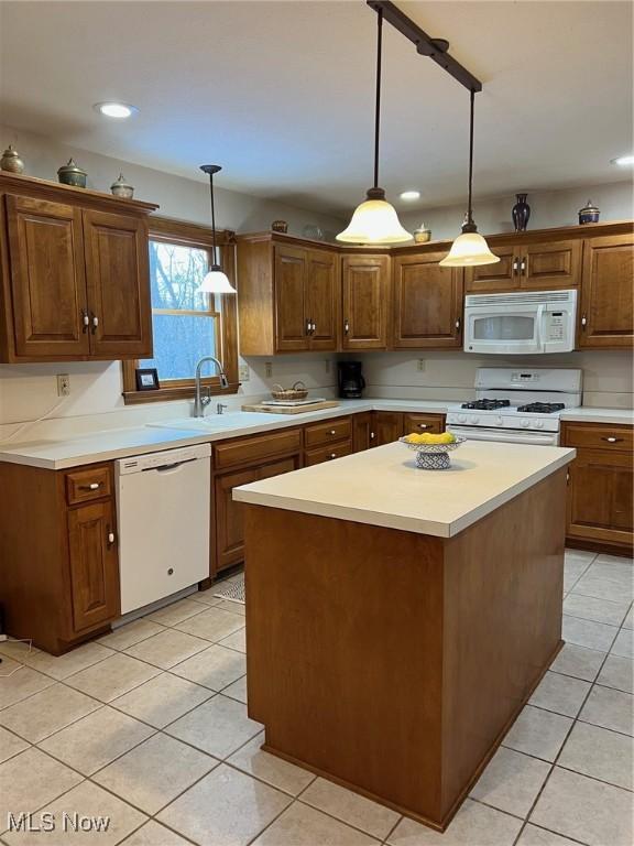 kitchen featuring hanging light fixtures, sink, light tile patterned floors, white appliances, and a center island