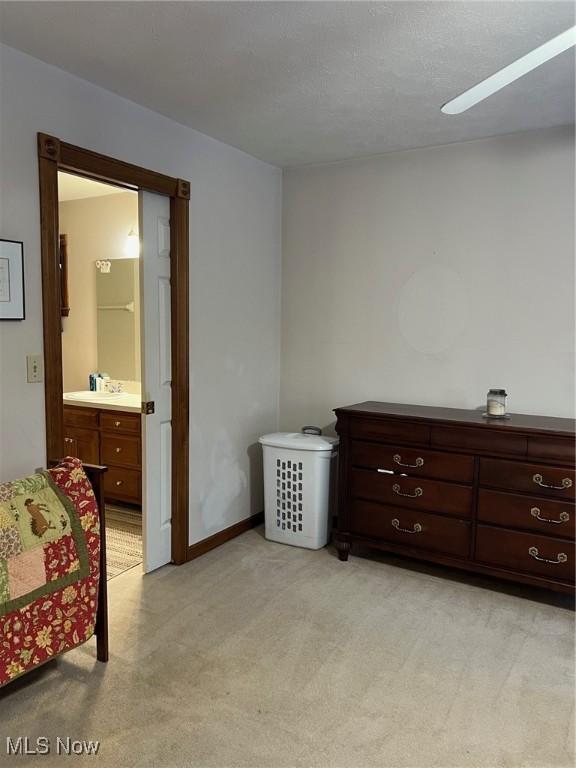 bedroom with sink, ceiling fan, light carpet, and ensuite bath