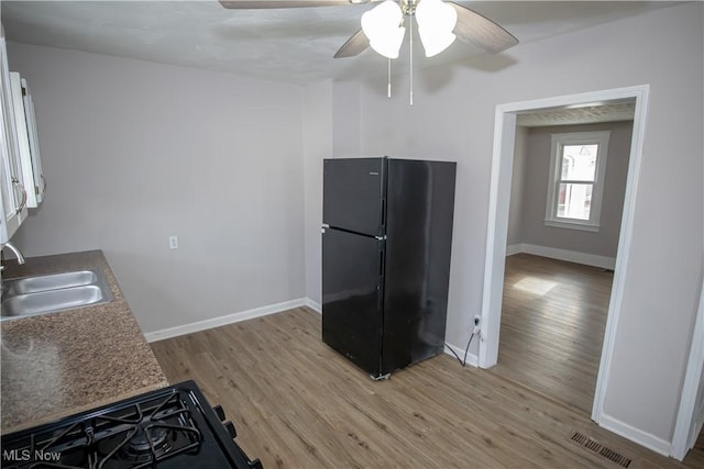 kitchen with black refrigerator, ceiling fan, sink, light hardwood / wood-style flooring, and stovetop