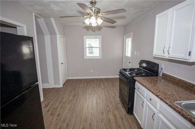 kitchen with black appliances, white cabinets, light hardwood / wood-style flooring, ceiling fan, and dark stone countertops