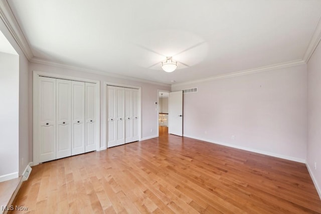 unfurnished bedroom with light hardwood / wood-style flooring, two closets, and ornamental molding