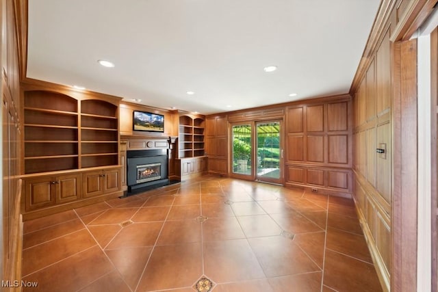 unfurnished living room featuring built in shelves, wood walls, tile patterned flooring, and ornamental molding