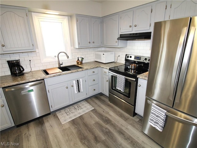 kitchen with appliances with stainless steel finishes, dark wood-style flooring, a sink, and under cabinet range hood