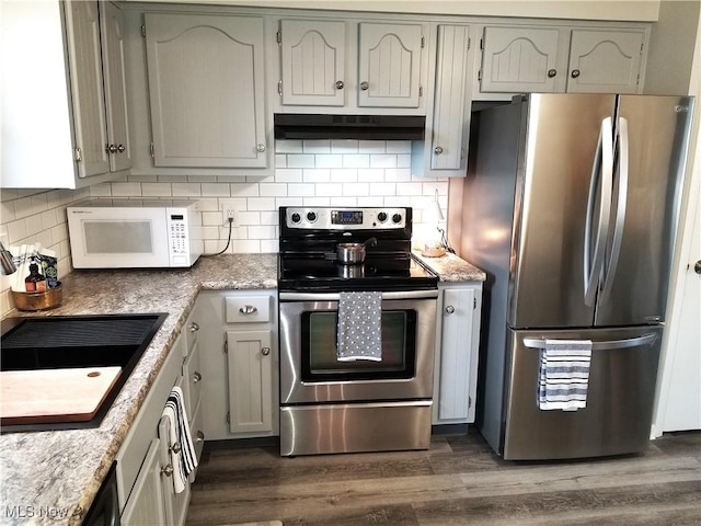 kitchen featuring decorative backsplash, dark wood-style floors, appliances with stainless steel finishes, under cabinet range hood, and a sink