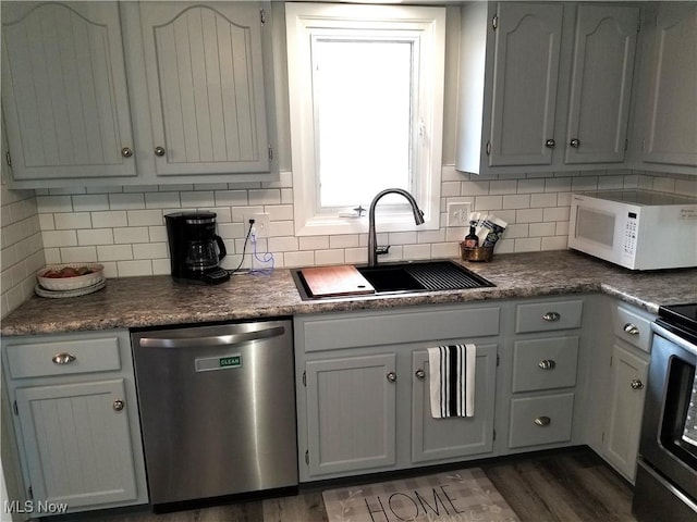 kitchen with white microwave, dark wood-style flooring, a sink, dishwasher, and tasteful backsplash