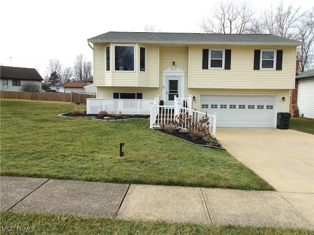 split foyer home featuring a garage, driveway, a front lawn, and fence