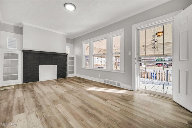 unfurnished living room with light wood-type flooring, a brick fireplace, and crown molding