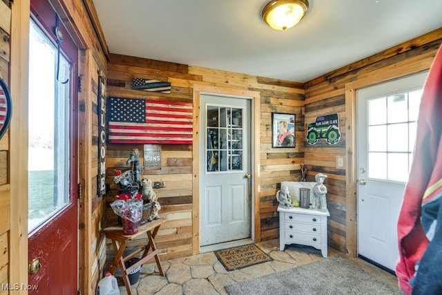 doorway to outside with light tile patterned floors, plenty of natural light, and wooden walls