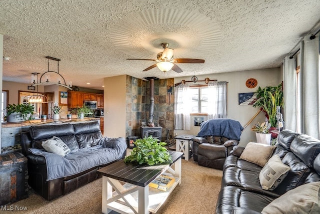 living room with ceiling fan, light colored carpet, a wood stove, and a textured ceiling