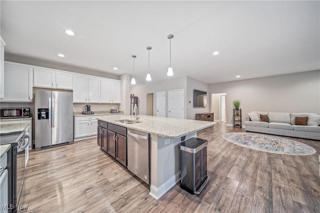 kitchen featuring a kitchen island with sink, white cabinets, hanging light fixtures, appliances with stainless steel finishes, and light stone counters