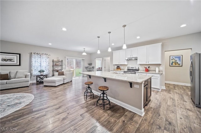 kitchen with light stone countertops, appliances with stainless steel finishes, decorative light fixtures, white cabinets, and a kitchen island