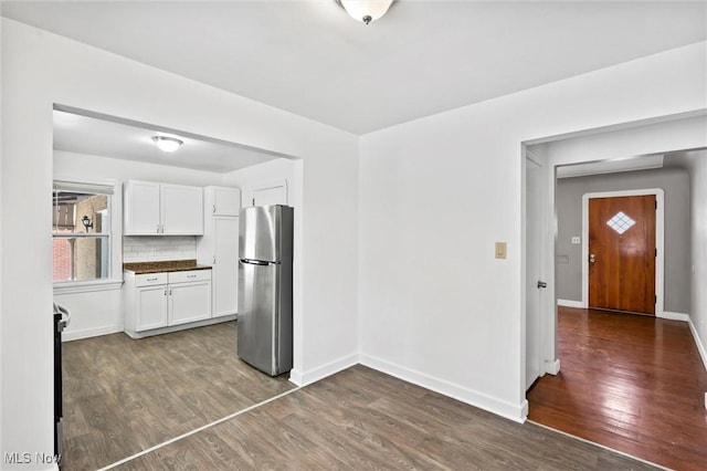 kitchen featuring stove, backsplash, dark wood-type flooring, white cabinets, and stainless steel refrigerator