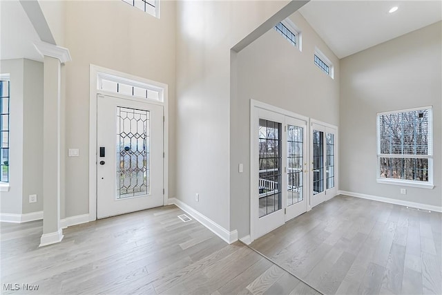 foyer entrance with a towering ceiling, french doors, and light hardwood / wood-style flooring