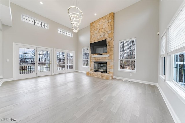 unfurnished living room featuring a fireplace, a towering ceiling, a chandelier, and light hardwood / wood-style floors