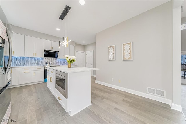 kitchen featuring hanging light fixtures, white cabinets, backsplash, a kitchen island, and appliances with stainless steel finishes