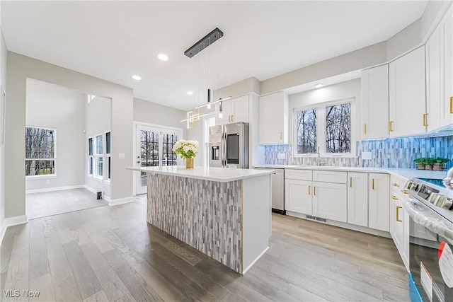 kitchen with white cabinetry, stainless steel appliances, backsplash, pendant lighting, and a kitchen island