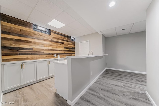 bar featuring a paneled ceiling, wooden walls, light hardwood / wood-style flooring, and white cabinets