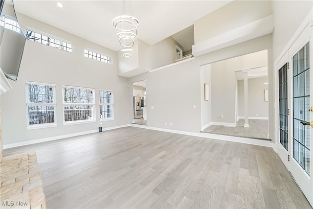 unfurnished living room with a chandelier, a high ceiling, and light hardwood / wood-style flooring