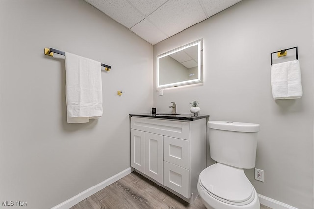 bathroom with a paneled ceiling, hardwood / wood-style floors, vanity, and toilet