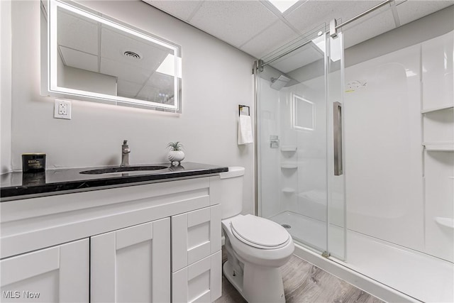 bathroom featuring a paneled ceiling, vanity, a shower with door, hardwood / wood-style floors, and toilet